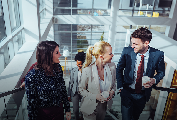 A low-angle view of business professionals in suits walking up a flight of stairs in a modern office building.