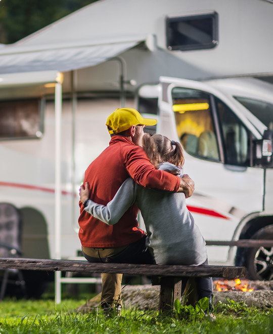 Happy couple hugging by their parked motorhome, representing RV and travel trailer insurance for road trips.