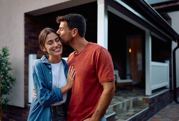 A joyful couple embracing outside their suburban home, celebrating the milestone of homeownership.