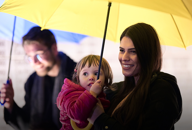 Happy family holding umbrellas in front of their home, representing umbrella liability insurance protection.