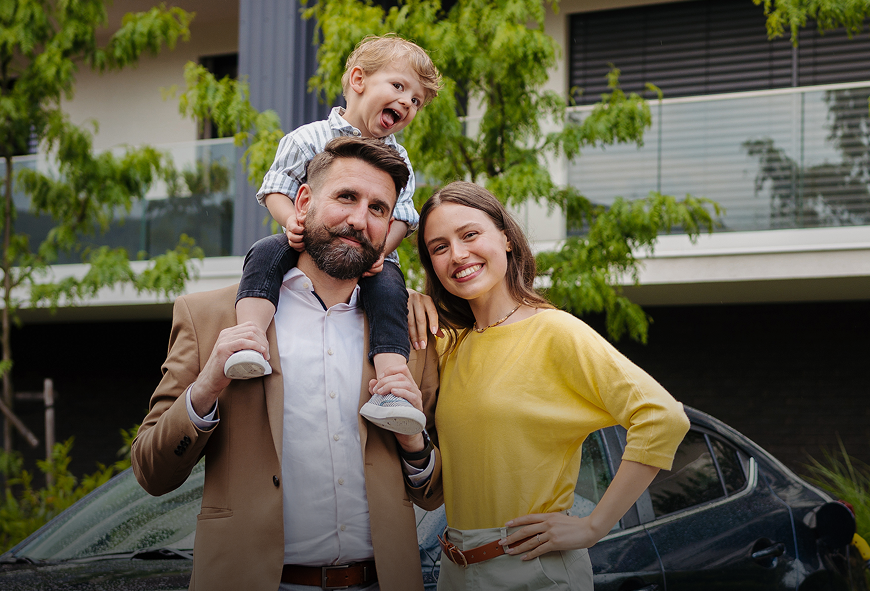 Happy family standing together near their car, representing comprehensive auto insurance.