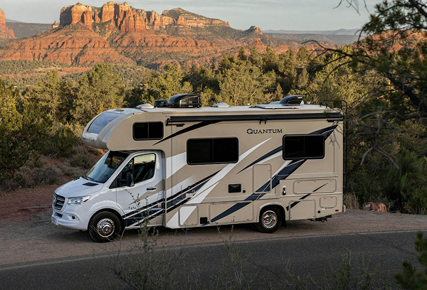 A modern motorhome parked in a vast desert landscape under a clear sky, surrounded by distant mountains and sparse vegetation.